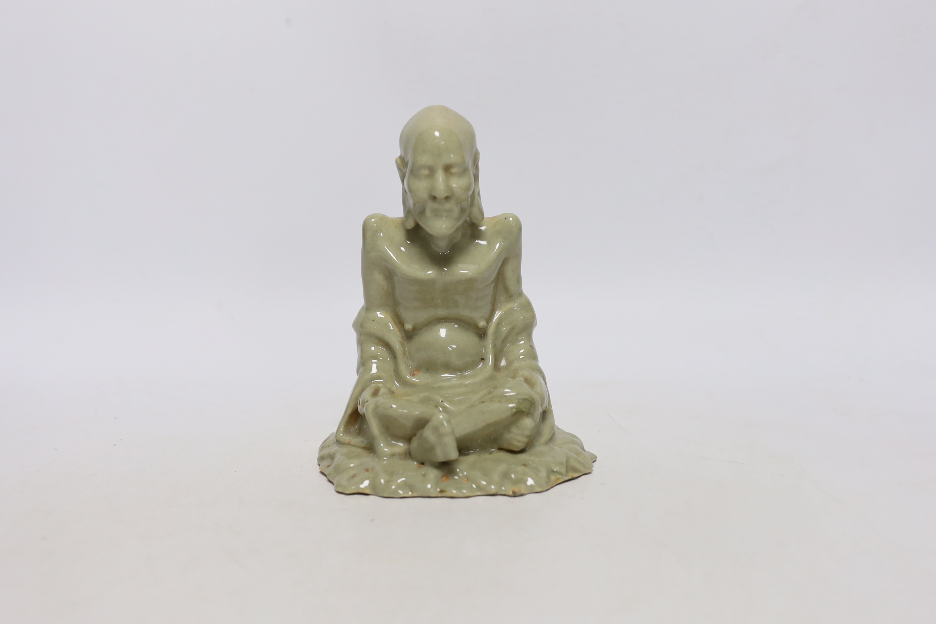 A Chinese celadon glazed figure of Laozi, 18th / 19th century, cross-legged and seated on leaves, 15cm high